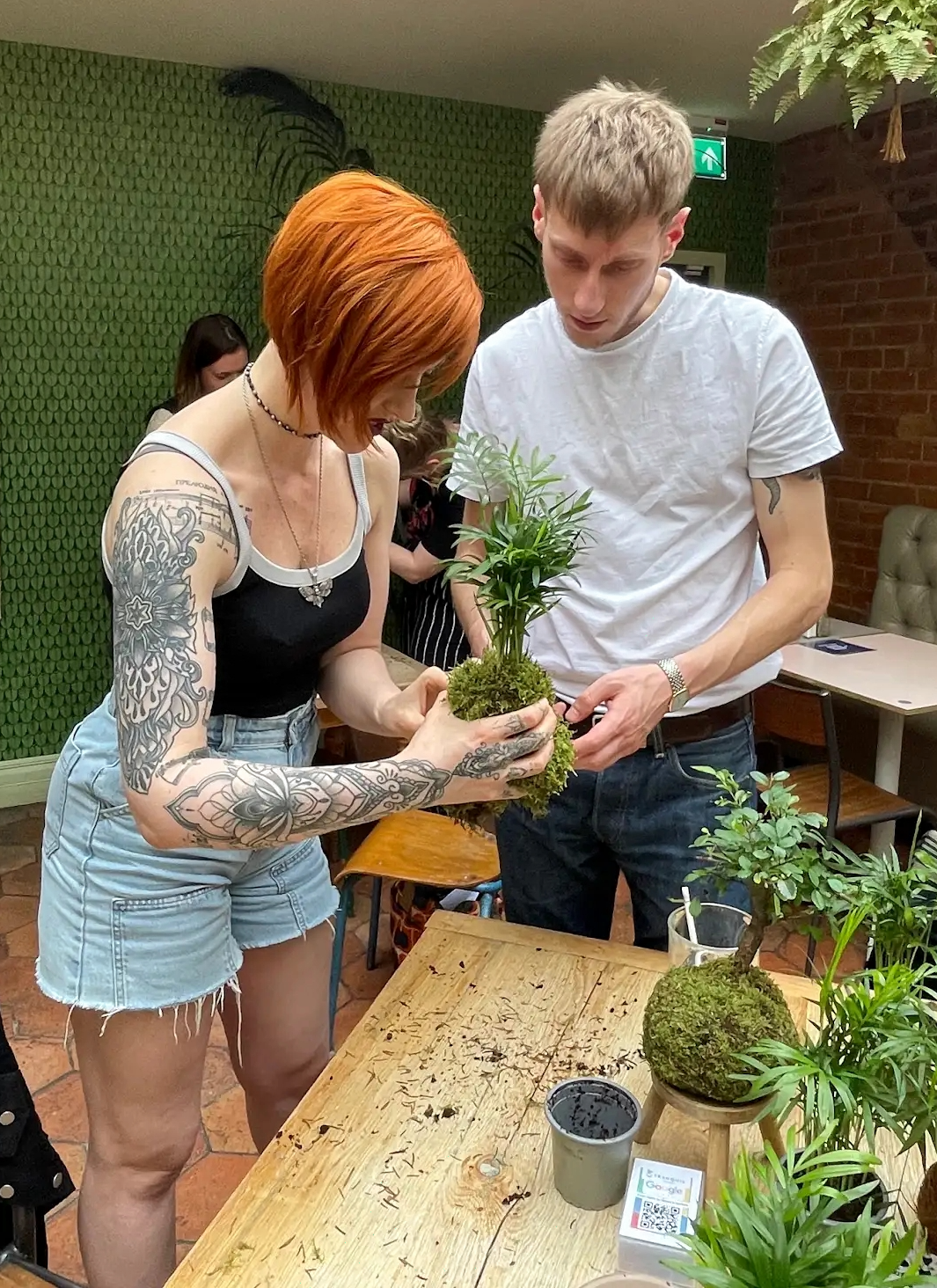 Two people, a man and a woman making  a palm wrapping moss around the base. 
